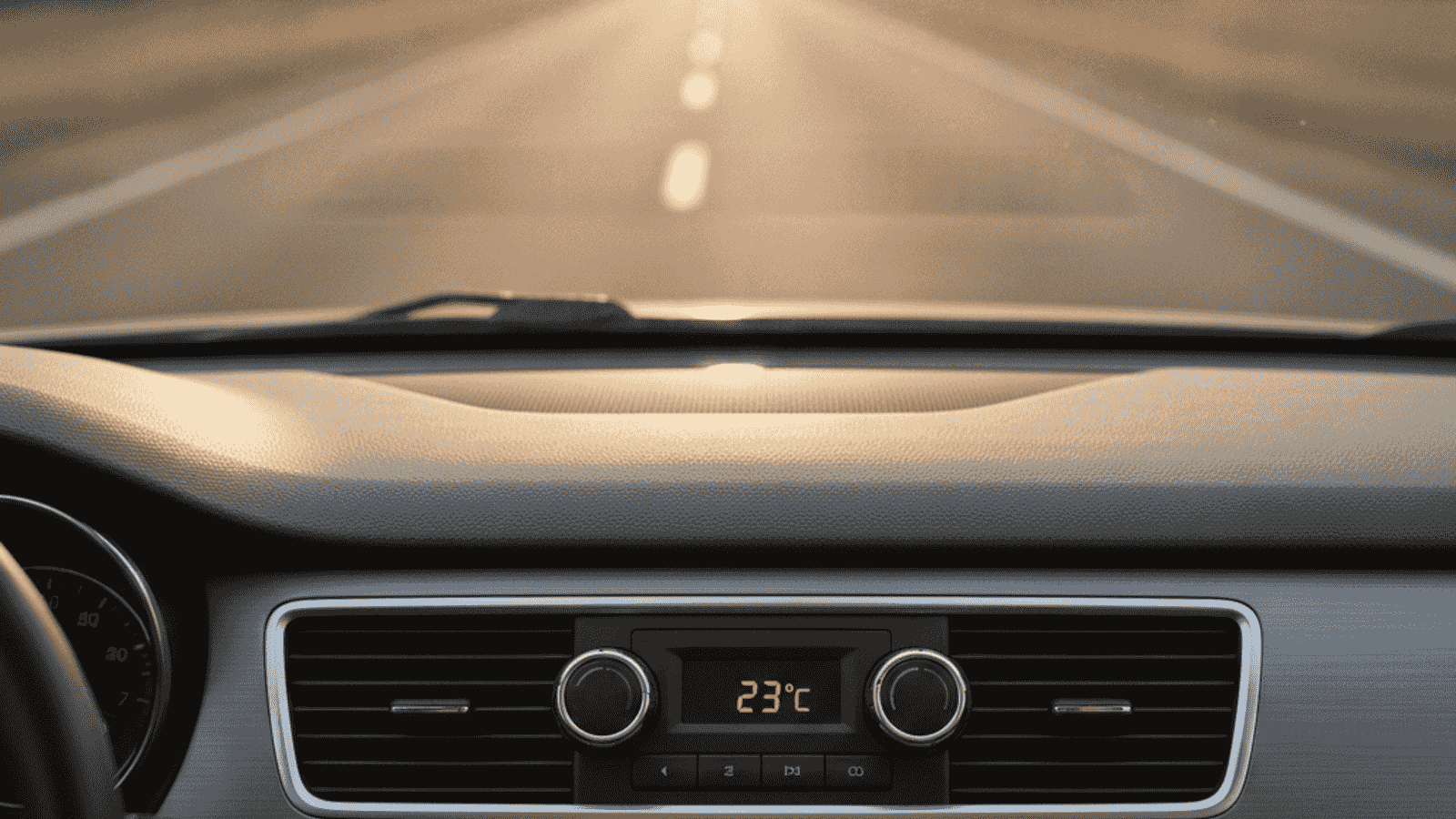 Car air conditioning controls on the dashboard under warm summer sun, view from the driver seat through the windshield onto a sunny summer road