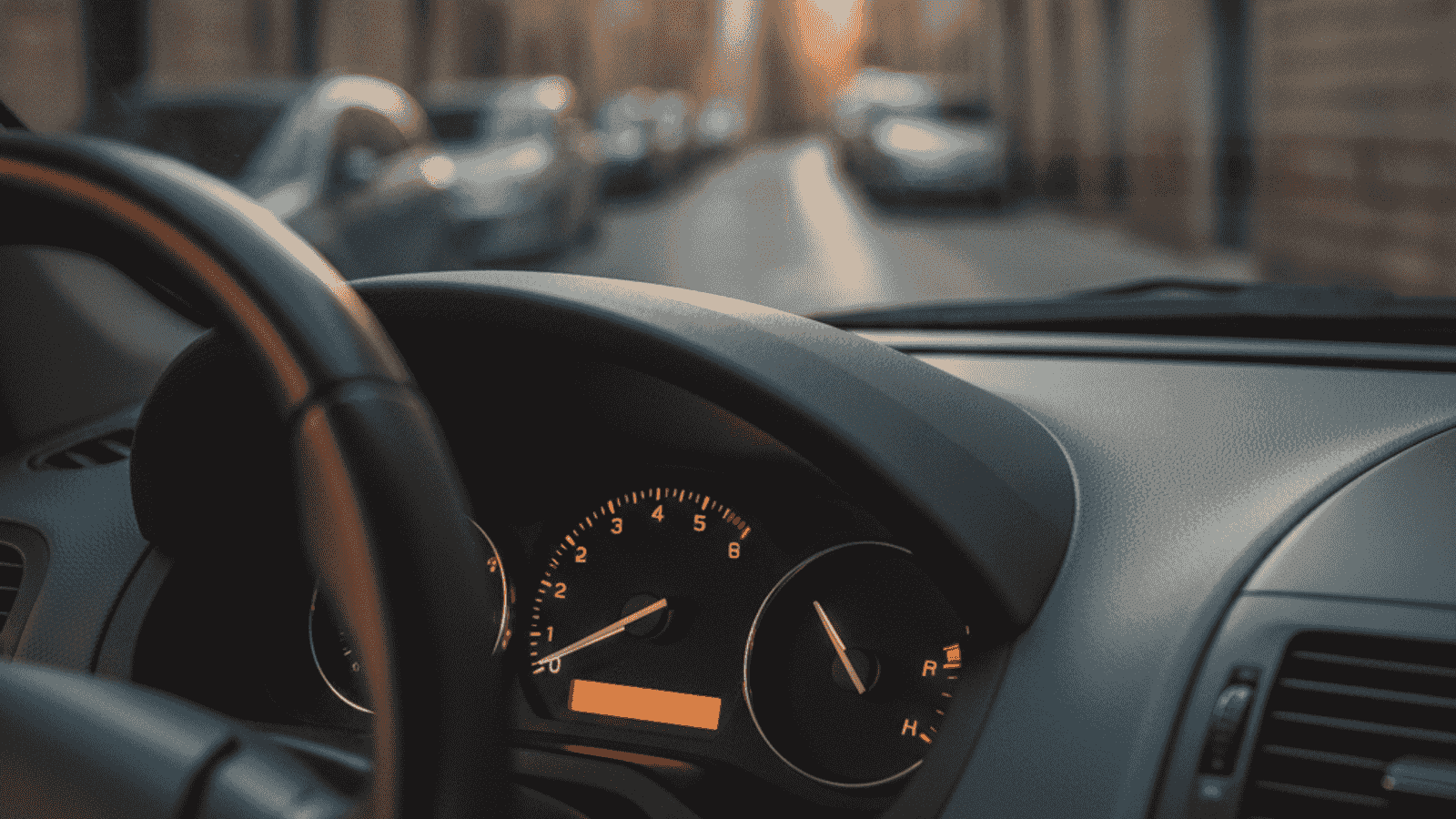 Instrument tabla automobila sa iglom temperature motora blizu hladne oznake, kroz vjetrobransko staklo vidi se kratka gradska ulica u jutarnjem svjetlu