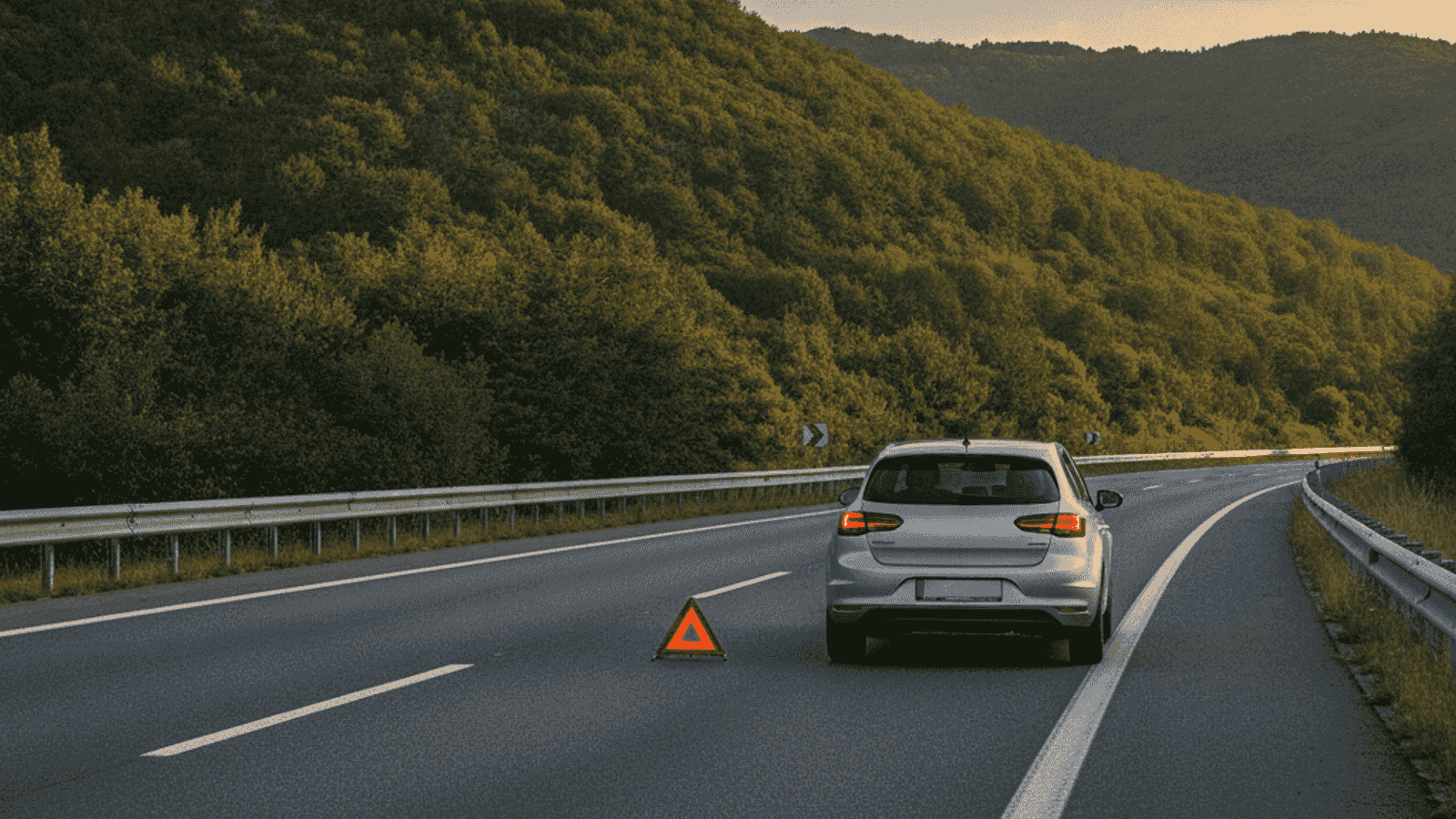 Car stopped on the hard shoulder of a motorway with hazard lights on and a warning triangle placed behind it