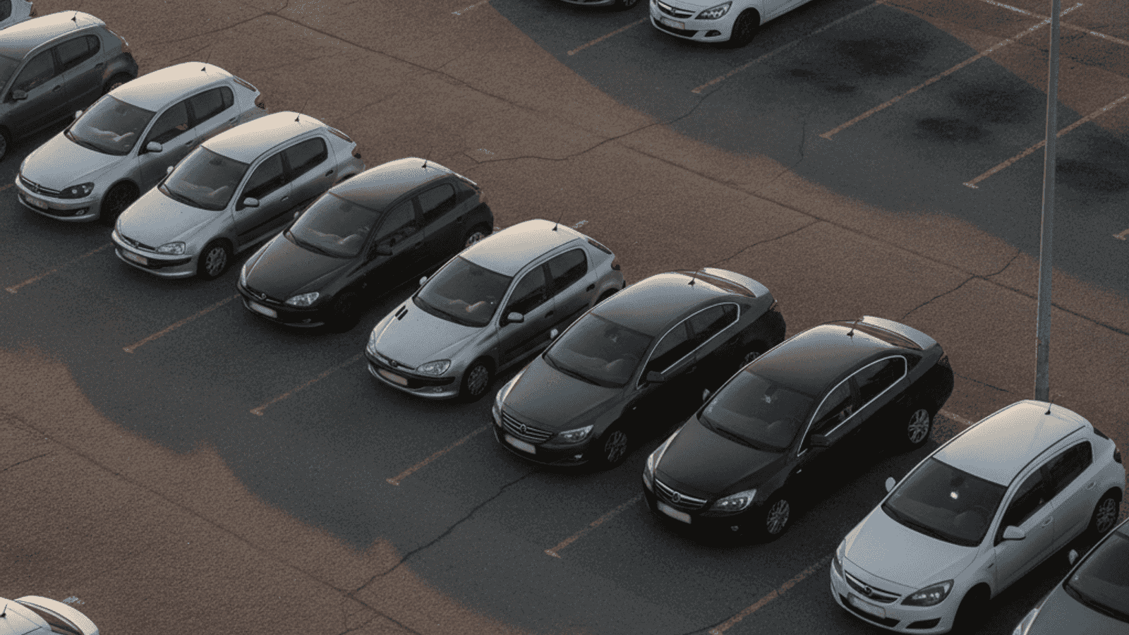 Pogled iz ptičje perspektive na parking sa mješavinom starijih i novijih automobila pod toplim poslijepodnevnim suncem