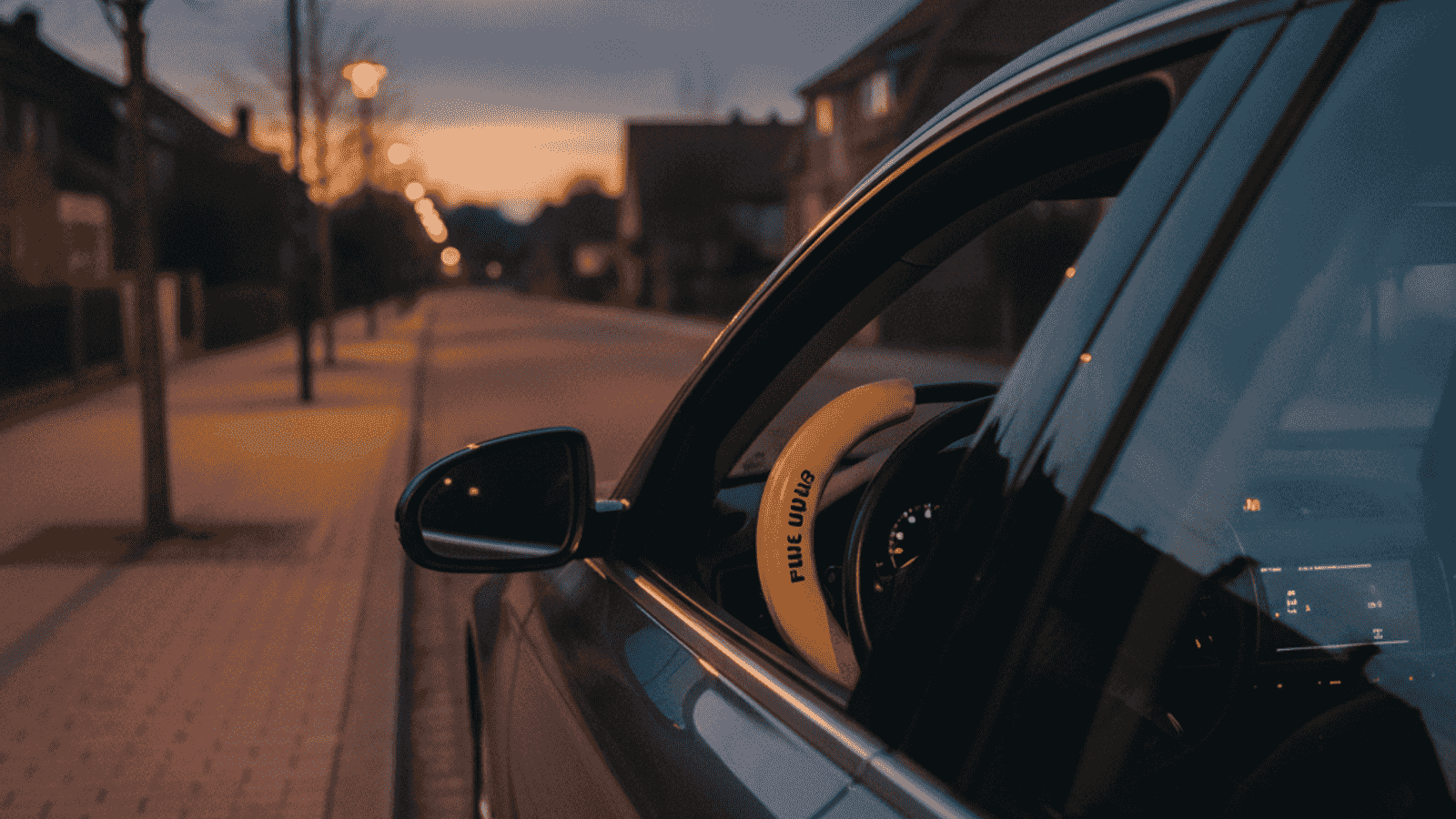 Dark European sedan parked at dusk with a visible yellow steering wheel lock as anti-theft protection